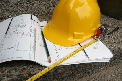 Hard hat on plans with a pencil and a measuring tape